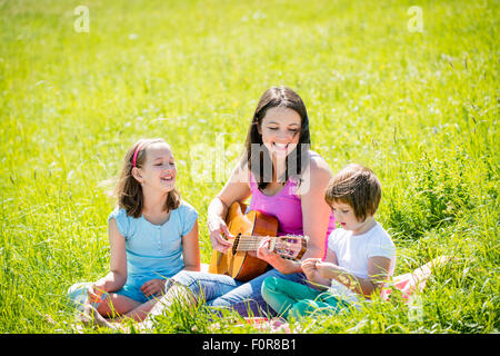 Femme jouant de la guitare à ses enfants dans la nature aux beaux jours d'été Banque D'Images