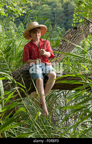 Jeune garçon habillé en pêche Huckleberry Finn assis dans un arbre Banque D'Images