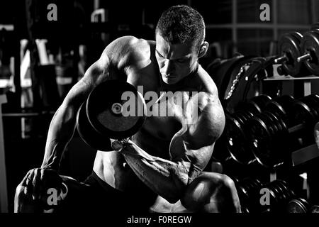 Puissance très sportif bodybuilder , exécuter l'exercice avec haltères courtes, dans le noir de sport, photo en noir et blanc Banque D'Images