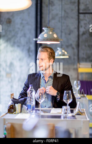 Chemise homme boutonnant dans un restaurant alors qu'il était assis à la table avec lampes suspendues Banque D'Images