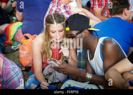 Jeune couple de course mixte à un festival, utilisant un téléphone mobile, Londres, Angleterre, Royaume-Uni. (jeune couple uk mixte race). Ensemble. Banque D'Images
