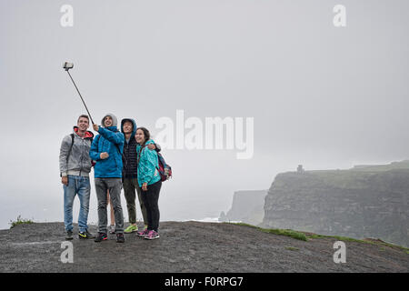 Groupe de personnes qui prend un avec un bâton selfies selfies à les falaises de Moher en Irlande Banque D'Images