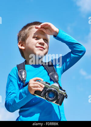 Petit garçon avec un appareil photo reflex rétro sur bleu ciel semble dans la distance Banque D'Images