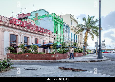 Un homme sur des béquilles passe devant un restaurant aux couleurs pastels sur le Malecon front de mer de La Havane Cuba Banque D'Images