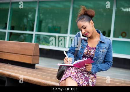 Jeune femme écrit dans son journal, tandis que sur le téléphone Banque D'Images