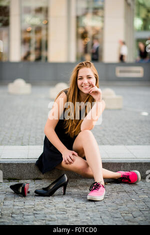 Jeune femme sur rue dans sneakers holding High heels shoes Banque D'Images