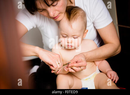 Coupe ongles sur les mains de la mère de son bébé - sitting on floor in bathroom Banque D'Images