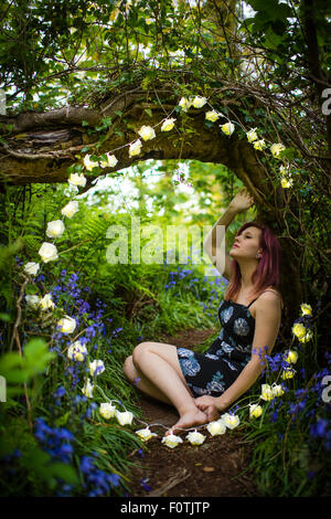 Fantasmes de fées : Une jeune femme adolescente seule par elle-même assis porte une robe dans les bois entouré d'une guirlande de fleurs blanc circulaire lumières, soirée d'UK Banque D'Images