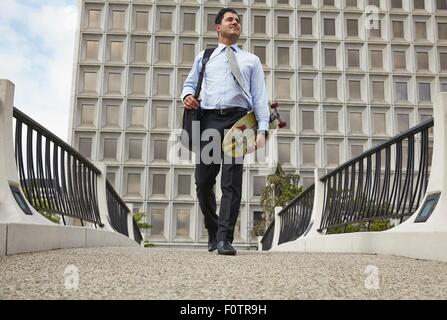 Toute la longueur de l'angle faible vue avant du milieu de l'adult business man carrying skateboard Banque D'Images