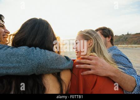 Groupe d'amis assis ensemble à la plage, au coucher du soleil, vue arrière Banque D'Images