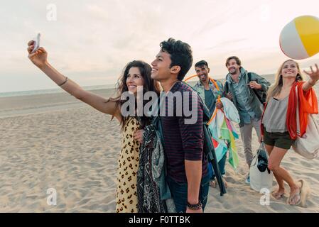 Groupe d'amis à marcher le long beach, young couple taking self portrait with smartphone Banque D'Images