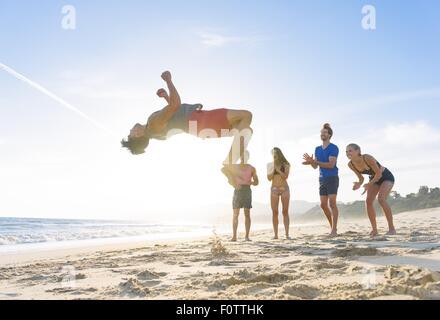 Groupe d'amis sur plage en regardant ami n'somersault Banque D'Images