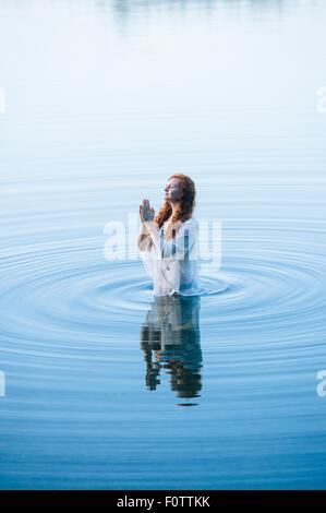 Jeune femme debout dans le lac ondulations avec les yeux fermés et les mains Banque D'Images