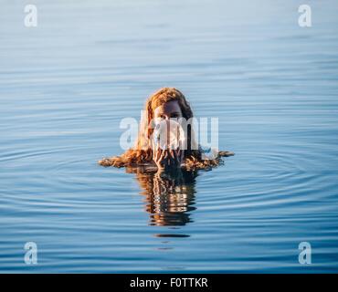 Tête et épaules de jeune femme aux longs cheveux rouges dans le lac holding crystal ball Banque D'Images