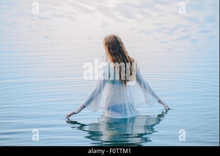 Vue arrière du young woman standing in lake surface ondulée avec ses doigts Banque D'Images