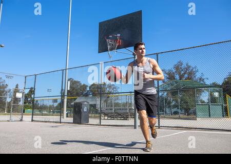 Jeune joueur de basket-ball masculin exécutant avec balle sur un terrain de basket-ball Banque D'Images