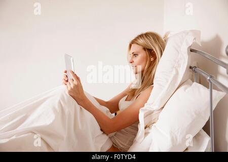Mid adult woman sitting up in bed using digital tablet