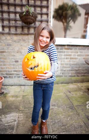 Smiling girl holding heavy halloween citrouille dans jardin Banque D'Images