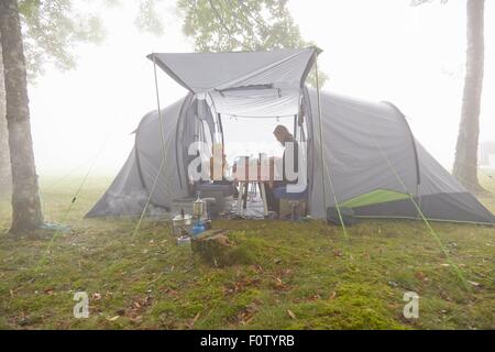 Mère et fils de prendre le petit déjeuner dans la tente dans un paysage brumeux Banque D'Images