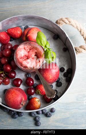 Verre de sorbet aux fruits servi avec des fruits frais et garnir de basilic Banque D'Images