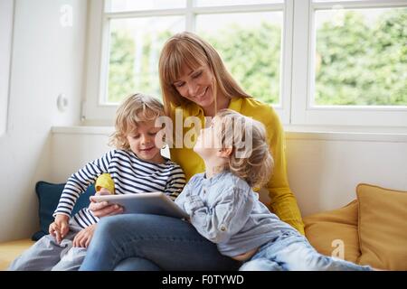La mère et les deux fils, assis à la fenêtre, looking at digital tablet Banque D'Images