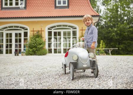 Garçon jouant avec vintage toy voiture en face de la maison Banque D'Images