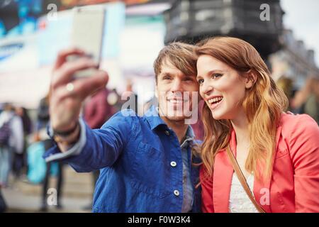 Couple de touristes prenant sur smartphone selfies à Piccadilly Circus, Londres, UK Banque D'Images