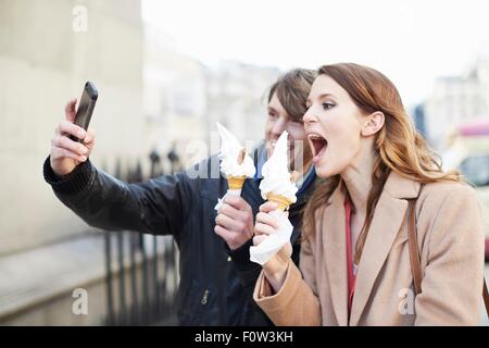 Couple avec ice cream cones en tenant selfies smartphone, London, UK Banque D'Images