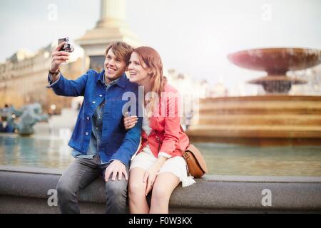 Couple qui selfies caméra à Trafalgar Square fontaine, Londres, Royaume-Uni Banque D'Images