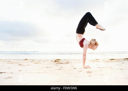 Mid adult woman practicing yoga position handstand on beach Banque D'Images