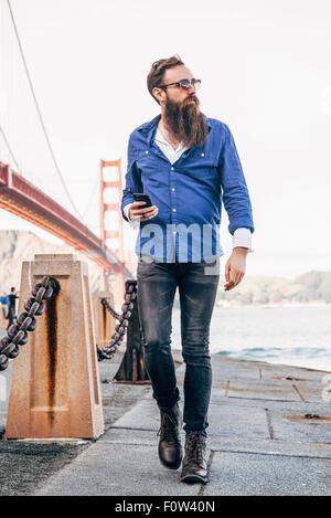 Homme avec barbe contrôle smartphone à Golden Gate Bridge, San Francisco, California, USA Banque D'Images