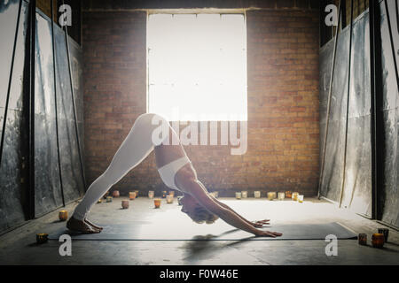 Une femme blonde se pencher sur le sol entourée de bougies, stretching. Une fenêtre dans le mur de brique derrière elle. Banque D'Images