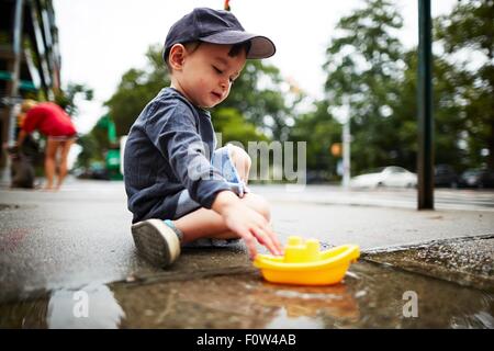 Boy Playing with toy voile sur l'eau sur la chaussée Banque D'Images