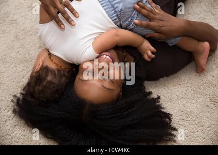 Mid adult woman hugging toddler fille on rug Banque D'Images