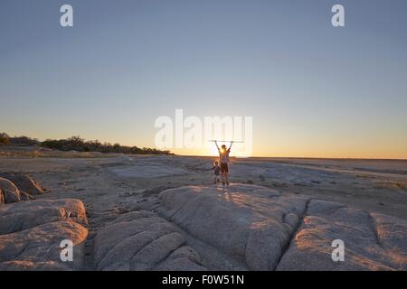 Deux garçons debout sur un rocher, tenant la lance dans l'air, le coucher du soleil, Gweta, makgadikgadi, Botswana Banque D'Images