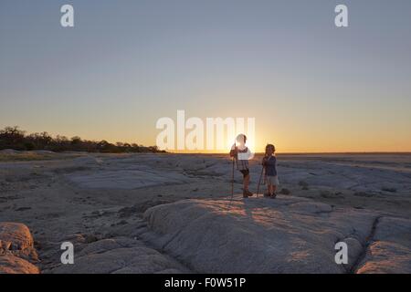 Deux garçons debout sur un rocher, tenant une lance, coucher de soleil, Gweta, makgadikgadi, Botswana Banque D'Images