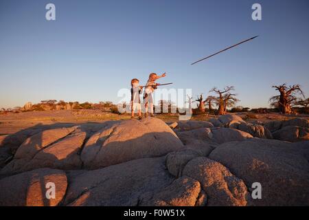 Deux jeunes garçons debout sur la roche, de lancer des piques, Gweta, makgadikgadi, Botswana Banque D'Images