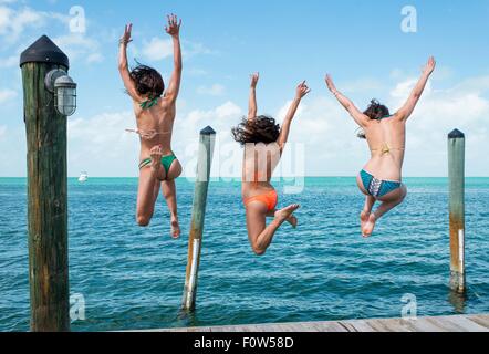 Vue arrière de trois jeunes femme sautant d'une mer pier, Islamorada, Florida, USA Banque D'Images