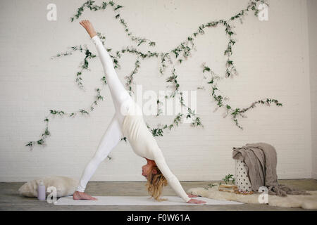 Une femme blonde dans un collant blanc et des jambières, debout sur un tapis blanc dans une chambre, se pencher vers le bas, la jambe relevée. Banque D'Images