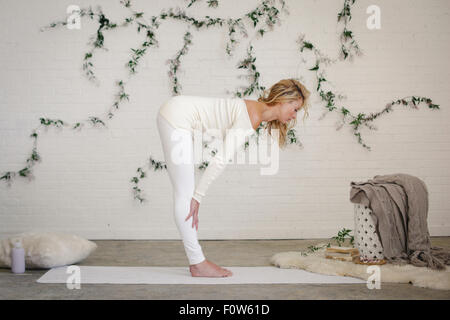 Une femme blonde dans un collant blanc et des jambières, debout sur un tapis blanc dans une chambre, se pencher vers l'avant. Banque D'Images