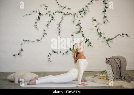 Une femme blonde dans un collant blanc et des jambières, couché sur un tapis blanc dans une chambre, se cambrant il retour dans un tronçon. Banque D'Images