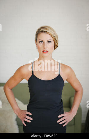 Une femme blonde dans un justaucorps noir debout dans une salle, faire du yoga, ses mains sur ses hanches, regardant la caméra. Banque D'Images