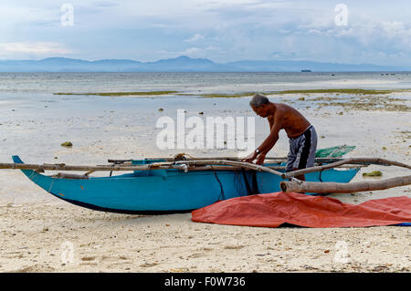 Un pêcheur nettoie son bateau. Lorsque l'eau a reculé vers l'extérieur, un pêcheur prépare son bateau pour la pêche lorsque l'eau revient plus tard Banque D'Images