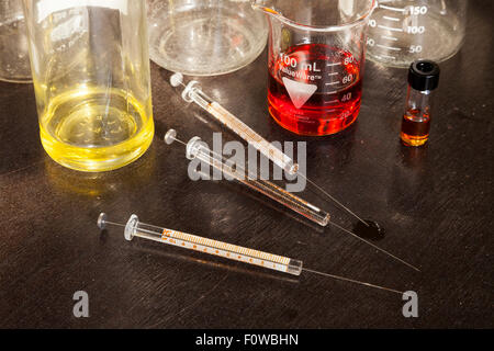 Béchers remplis de liquides colorés et seringues en verre assis sur une table. Banque D'Images