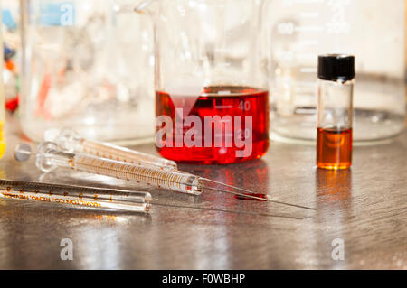 Béchers remplis de liquides colorés et seringues en verre assis sur une table. Banque D'Images