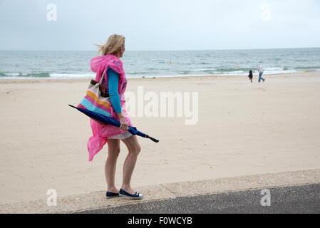 Vacancier femelle avec un parapluie et poncho au bord de la mer, sur un jour pluvieux et venteux. Le sud de l'Angleterre Bournemouth, Royaume-Uni Banque D'Images