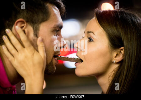 Jeune couple de manger ensemble un morceau de chocolat - dans la rue la nuit Banque D'Images