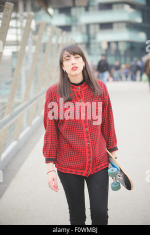 Belle jeune femme de race blanche en se promenant dans les rues de la ville avec une planche à roulettes à poser et à la jeunesse, à huis clos - Banque D'Images