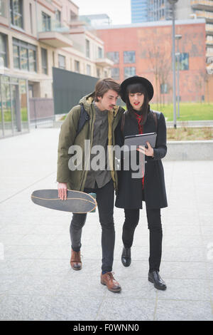 Couple de jeunes belle femme et l'homme, avec moustache et skate, randonnée pédestre à travers la ville à l'aide d'une tablette - technologie, social Banque D'Images