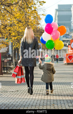 Femme heureuse et petit enfant avec sac shopping rouge et air-ballons, de marcher sur la rue Banque D'Images